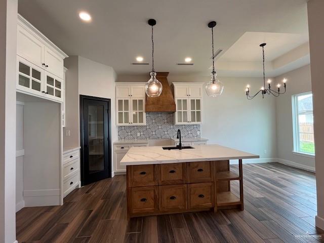 kitchen with white cabinetry, pendant lighting, a center island with sink, and tasteful backsplash