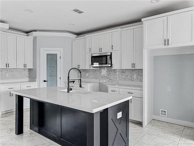 kitchen with sink, light stone counters, backsplash, a center island with sink, and white cabinets