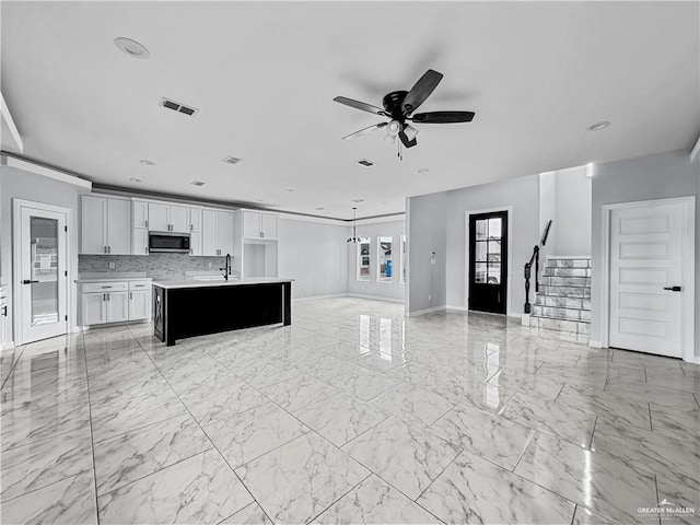 kitchen with a center island with sink, white cabinets, sink, ceiling fan, and tasteful backsplash