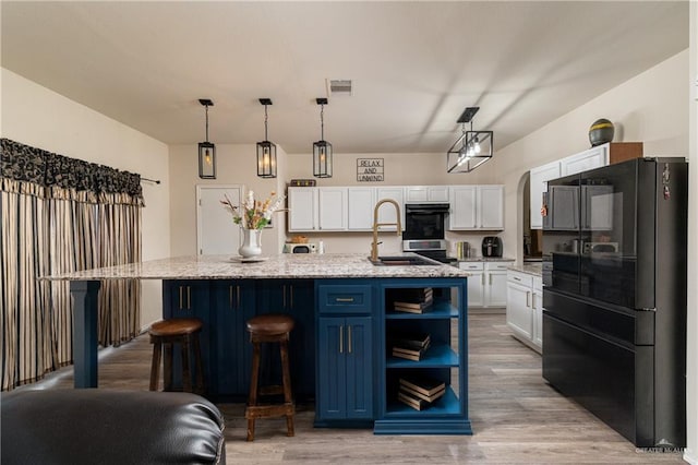 kitchen featuring a kitchen island with sink, pendant lighting, freestanding refrigerator, and white cabinets