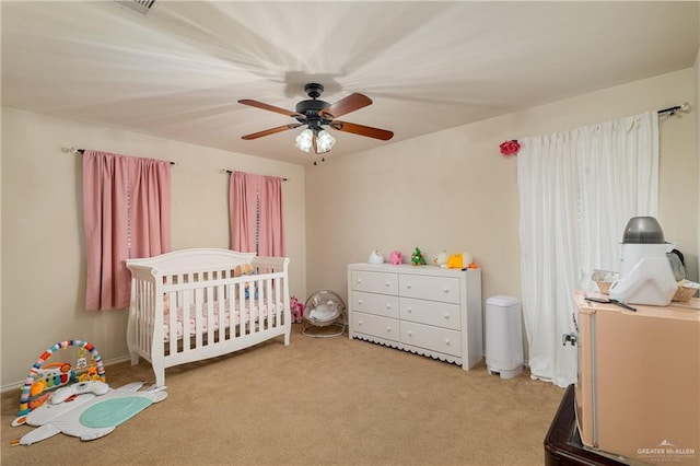 bedroom with a nursery area, visible vents, a ceiling fan, and light colored carpet