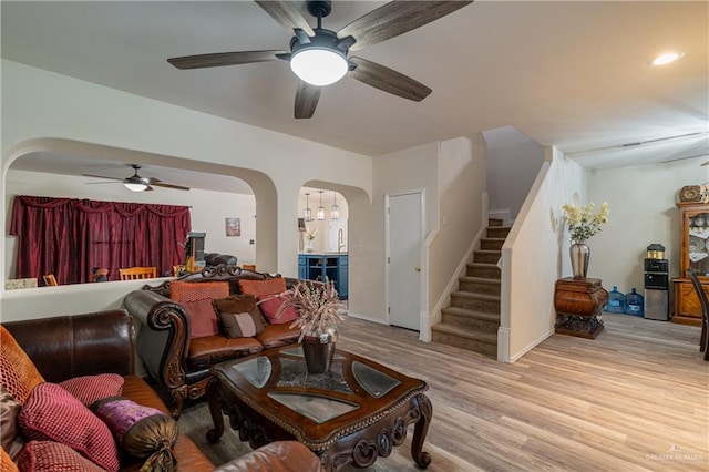 living room with stairs, light wood-type flooring, arched walkways, and a ceiling fan