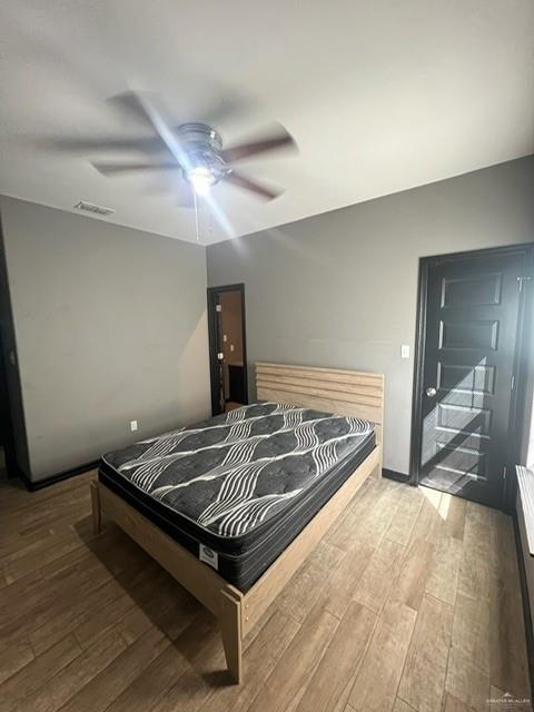 bedroom featuring ceiling fan, wood finished floors, visible vents, and baseboards