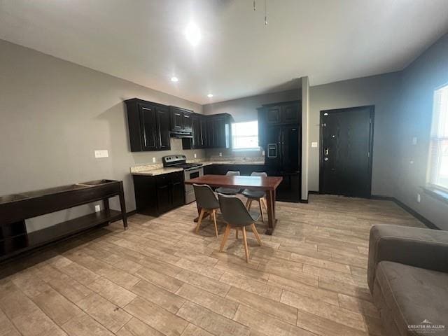 kitchen featuring light wood-style floors, stainless steel range with electric cooktop, light countertops, dark cabinetry, and black fridge