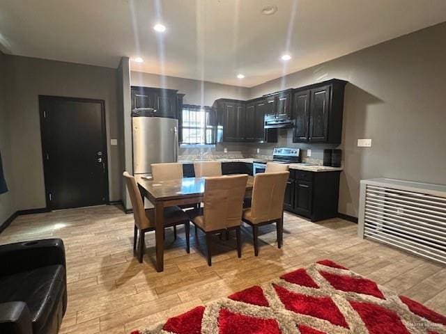 kitchen with light wood finished floors, appliances with stainless steel finishes, dark cabinets, range hood, and light countertops