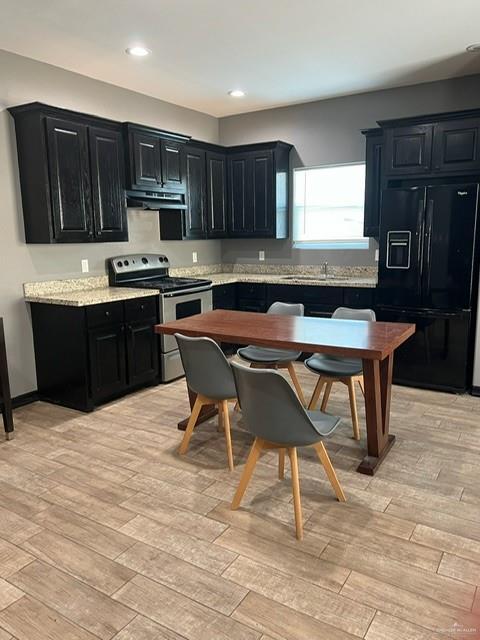 kitchen featuring dark cabinets, black fridge, under cabinet range hood, and stainless steel electric stove