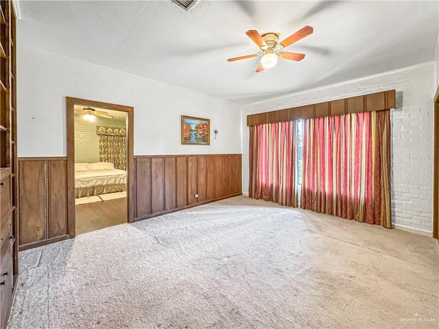 unfurnished room featuring light carpet, wooden walls, and ceiling fan