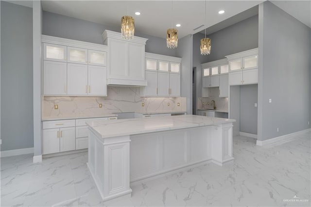 kitchen featuring light stone counters, hanging light fixtures, a center island, and white cabinets