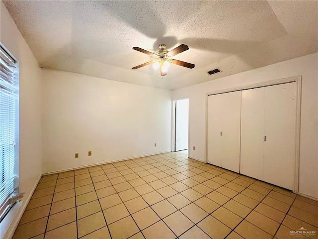 unfurnished bedroom with light tile patterned floors, a textured ceiling, a closet, and ceiling fan