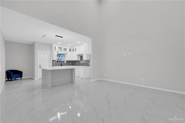 interior space with a kitchen island, white cabinets, backsplash, and decorative light fixtures