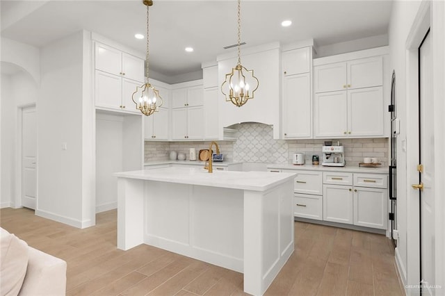 kitchen with light wood-type flooring, backsplash, a center island with sink, white cabinetry, and hanging light fixtures