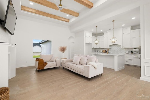 living room with beamed ceiling, a high ceiling, light hardwood / wood-style flooring, and sink