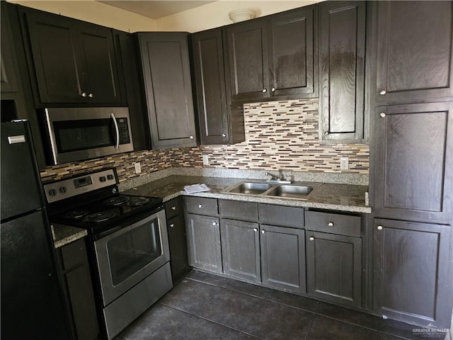 kitchen featuring sink, dark tile patterned floors, stainless steel appliances, light stone counters, and decorative backsplash