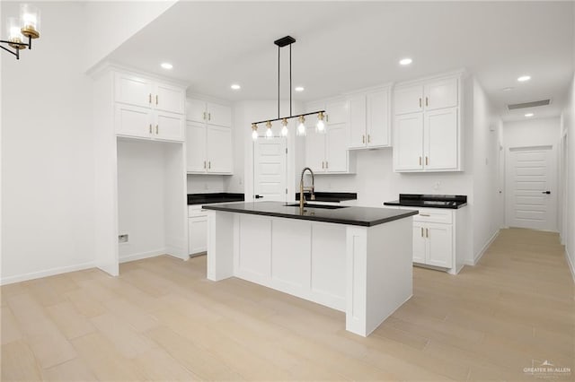 kitchen with pendant lighting, white cabinetry, a kitchen island with sink, and sink