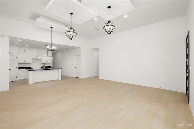 unfurnished living room featuring light hardwood / wood-style flooring, a towering ceiling, a chandelier, and sink