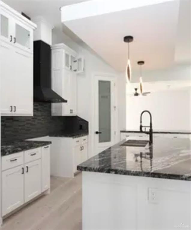 kitchen featuring decorative backsplash, dark stone counters, a sink, white cabinets, and glass insert cabinets