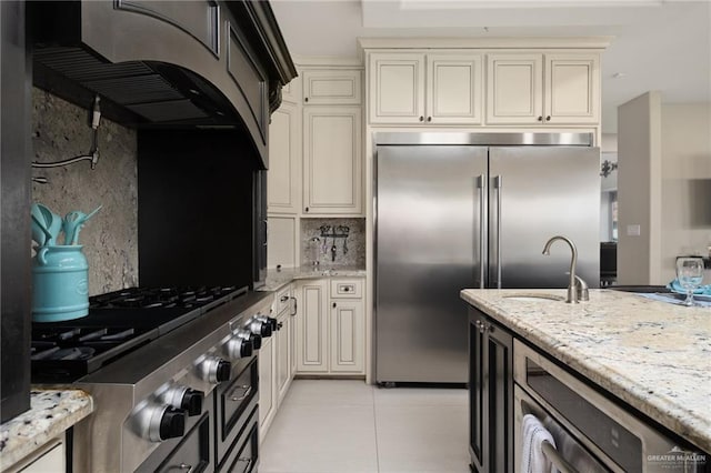 kitchen with cream cabinetry, light stone countertops, appliances with stainless steel finishes, and tasteful backsplash