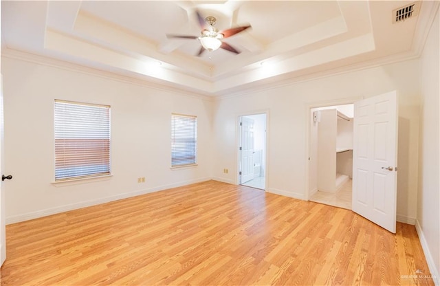 unfurnished bedroom featuring light wood-type flooring, a raised ceiling, baseboards, and crown molding