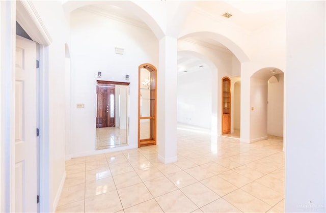 hall featuring a high ceiling, baseboards, visible vents, and ornamental molding