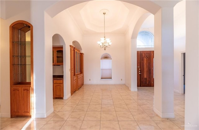 entryway with a high ceiling, an inviting chandelier, crown molding, light tile patterned floors, and a raised ceiling