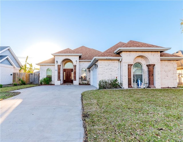 mediterranean / spanish-style home with driveway, a front lawn, fence, an attached garage, and a shingled roof