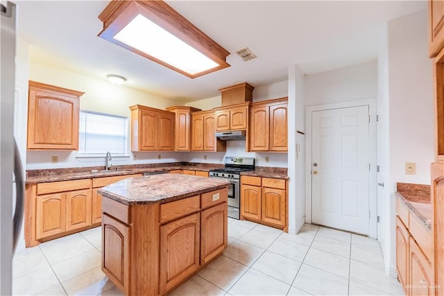 kitchen with under cabinet range hood, stone countertops, a sink, a center island, and stainless steel appliances