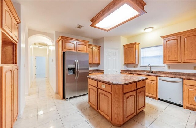 kitchen featuring a center island, arched walkways, stone countertops, stainless steel appliances, and a sink