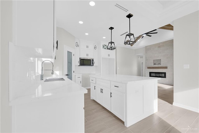 kitchen featuring sink, white cabinetry, hanging light fixtures, a center island, and a fireplace