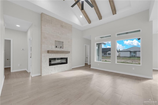 unfurnished living room featuring light hardwood / wood-style flooring, ceiling fan, high vaulted ceiling, a stone fireplace, and beamed ceiling