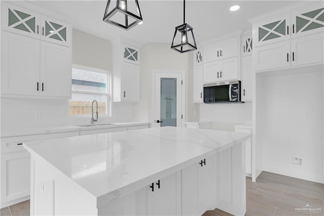 kitchen with pendant lighting, sink, light stone counters, white cabinets, and a kitchen island