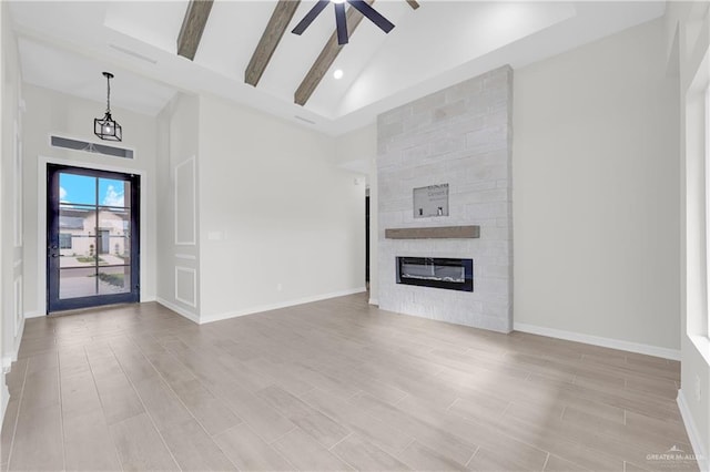 unfurnished living room with beamed ceiling, high vaulted ceiling, a fireplace, and light hardwood / wood-style flooring