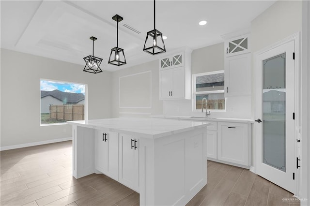 kitchen with sink, light stone counters, a kitchen island, pendant lighting, and white cabinets