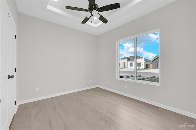 spare room with ceiling fan, a tray ceiling, and light hardwood / wood-style flooring