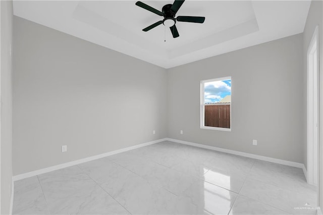 unfurnished room featuring a ceiling fan, a tray ceiling, and baseboards