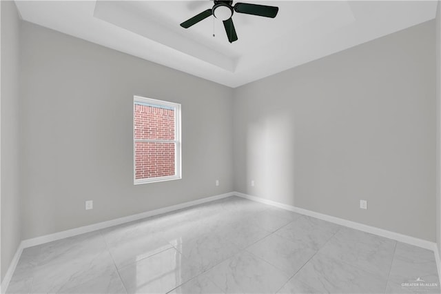 spare room featuring baseboards, a tray ceiling, and a ceiling fan