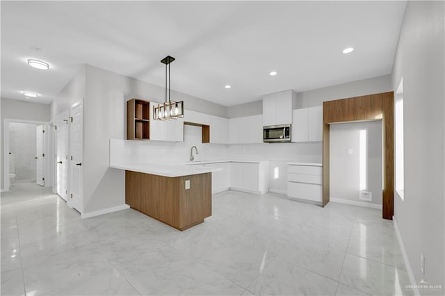 kitchen featuring stainless steel microwave, a peninsula, hanging light fixtures, white cabinetry, and a sink