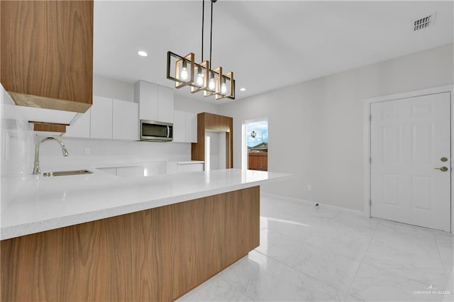 kitchen with a peninsula, a sink, visible vents, stainless steel microwave, and modern cabinets