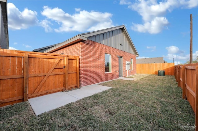 view of side of home with a lawn, a fenced backyard, a gate, board and batten siding, and brick siding