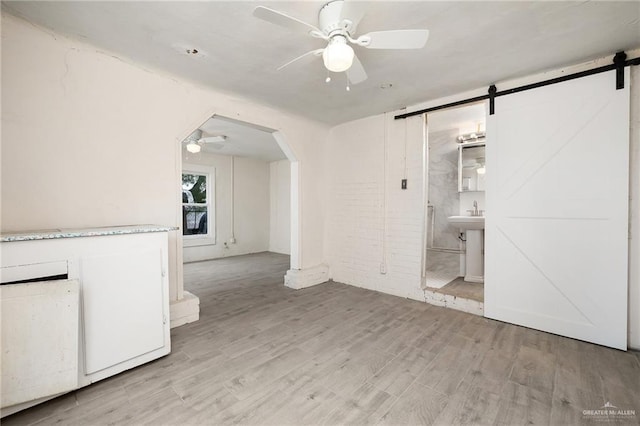 unfurnished living room featuring ceiling fan, a barn door, sink, and light hardwood / wood-style flooring