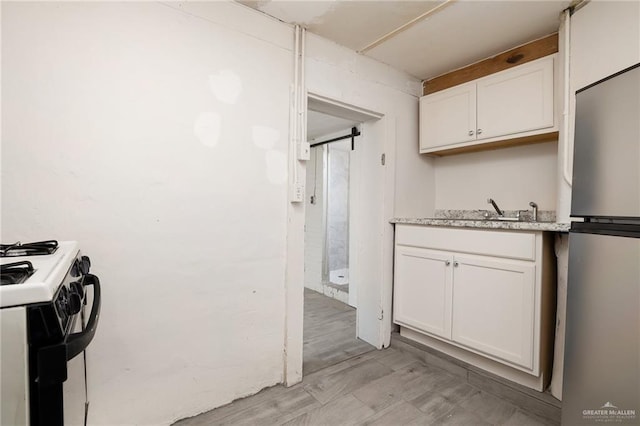 kitchen featuring stainless steel fridge, light wood-type flooring, white range oven, sink, and white cabinets