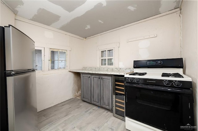 kitchen with gray cabinetry, beverage cooler, light hardwood / wood-style flooring, stainless steel refrigerator, and white gas stove