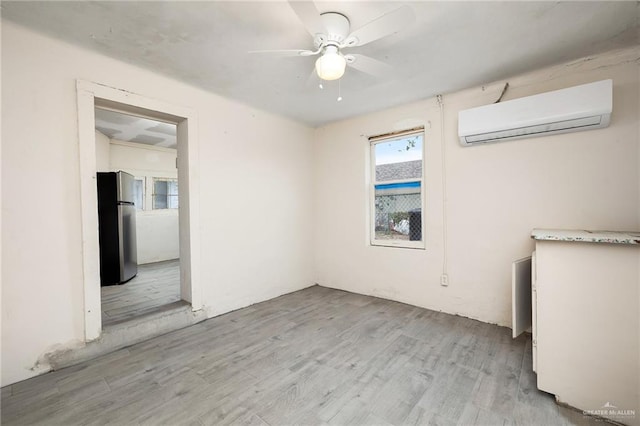 empty room with a wall mounted air conditioner, ceiling fan, and light wood-type flooring