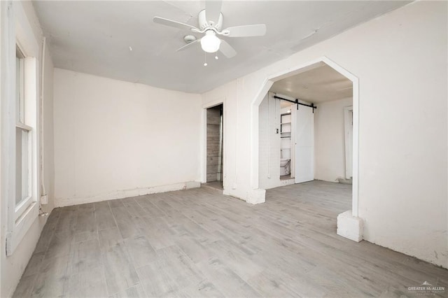 unfurnished room with a barn door, ceiling fan, and light hardwood / wood-style flooring