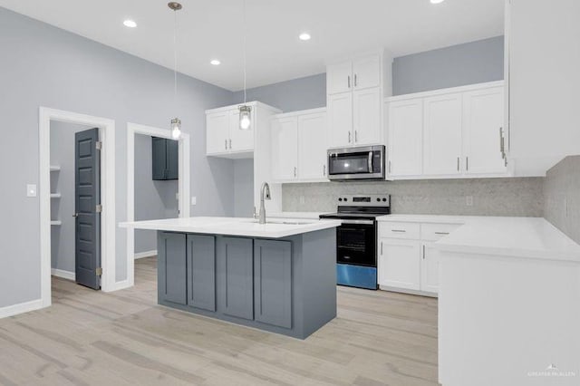 kitchen featuring light wood-type flooring, stainless steel appliances, decorative light fixtures, a center island with sink, and white cabinets