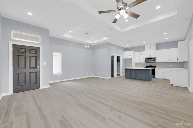 unfurnished living room with a raised ceiling, ceiling fan, and light wood-type flooring