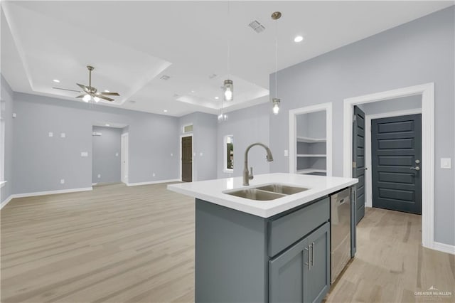 kitchen with dishwasher, a kitchen island with sink, a raised ceiling, hanging light fixtures, and sink