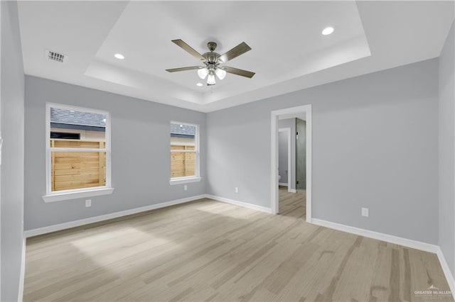 spare room with ceiling fan, a raised ceiling, and light wood-type flooring