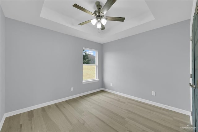 unfurnished room featuring a raised ceiling, ceiling fan, and light wood-type flooring