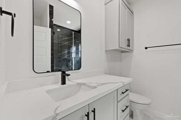 bathroom featuring toilet, tiled shower, and vanity