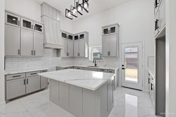 kitchen with gray cabinets, a center island, hanging light fixtures, light stone countertops, and sink